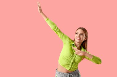 Güzel, genç, mutlu bir kadın pembe arka planda dans ediyor.