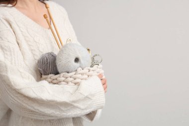 Hasır sepet tutan kadın örgü ipliği, iğneler ve gri arka planda mezura, yakın plan