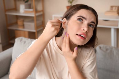 Evde kulak damlası kullanan genç bir kadın.