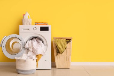 Çamaşır ve sepetli çamaşır makinesi sarı duvarın yanında.