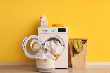 Çamaşır ve sepetli çamaşır makinesi sarı duvarın yanında.