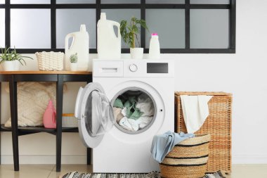 Çamaşır makinesi, deterjan ve sepetli çamaşır odasının içi.