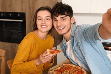 Pepperoni pizzalı genç çift mutfakta selfie çekiyor.
