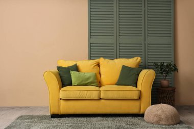 Sarı kanepe, katlanır ekran, puf ve çiçekli oturma odasının içi.