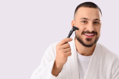 Beyaz arka planda tıraş bıçağı olan bornozlu genç bir adam.