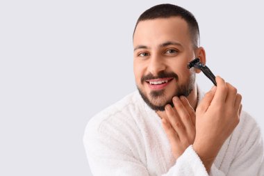 Beyaz arka planda tıraş bıçağı olan bornozlu genç bir adam.