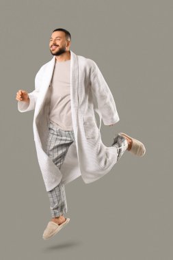 Gri arka planda atlayan bornozlu genç adam.