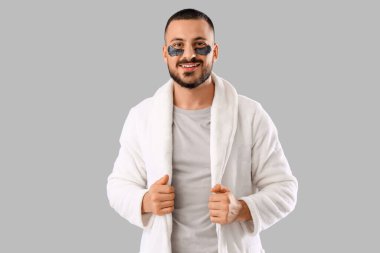 Gri arka planda göz bantları olan bornozlu genç bir adam.