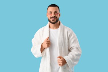 Mavi arka planda göz bantları olan cüppeli genç bir adam.