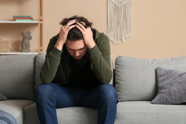 Depresyondaki genç adam evdeki kanepede oturuyor.