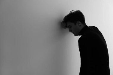 Aydınlık duvarın yanındaki depresif genç adamın siyah beyaz portresi