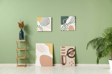 Sanat galerisindeki yeşil duvarın yanındaki rafta otlu vazolar ve güzel tablolar.