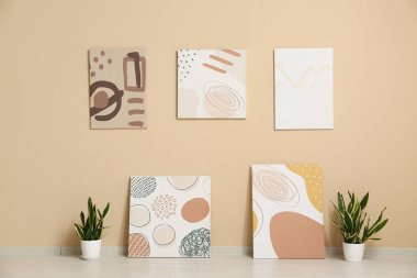 Sanat galerisinde bej duvarın yanında bitkiler olan güzel tablolar.