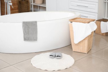 Modern banyo küvetinin yanında halının üzerinde yumuşak terlikler.