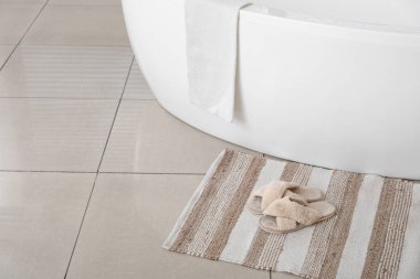 Modern banyo küvetinin yanında halının üzerinde yumuşak terlikler.