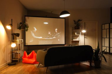 Geceleri projektör ekranlı, kanepeli ve armut çantalı karanlık oturma odasının içinde.