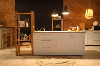 Beyaz tezgahlı mutfak, raf üniteleri ve akşamları parlayan lambalar.