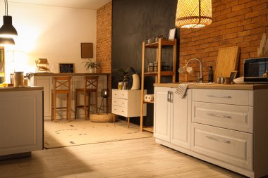 Beyaz tezgahlı mutfak, raf ünitesi ve akşamları parlayan lambalar.