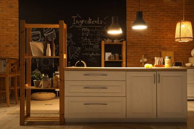 Akşamları beyaz tezgahlı, karatahtalı ve parlayan lambalı mutfağın içi.