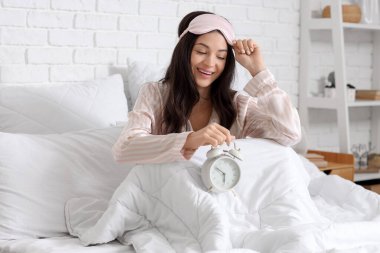 Yatak odasında uyku maskesi ve çalar saati olan genç bir kadın uyandı.