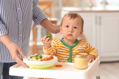 Anne bebeğini evdeki yüksek sandalyede sebzelerle besliyor.