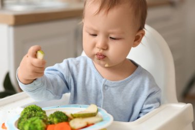 Evdeki yüksek sandalyede taze yemek yiyen şirin küçük bebek, yakın plan.