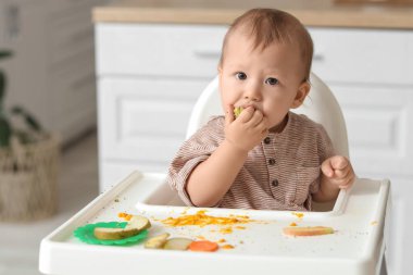Evde yüksek sandalyede yemek yiyen komik küçük bebek.