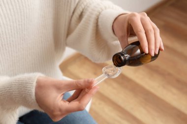 Elinde bir şişe öksürük şurubu ve evde kaşık ölçen bir kadın.