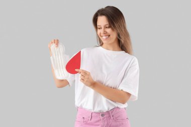 Aybaşı pedi ve arka planda kağıt kan damlası olan genç bir kadın.