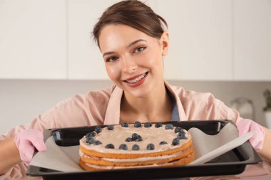 Kadın pastacı elinde kek tepsisiyle mutfakta, yakın plan.