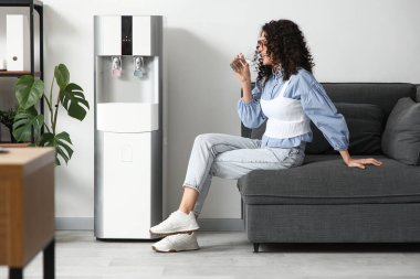 Ofisteki soğutucunun yanındaki koltukta su içen güzel kadın.