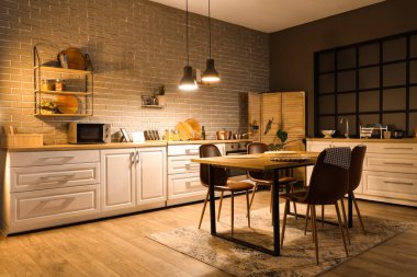 Mutfağın içinde tezgahlar, yemek masası ve akşam lambaları var.