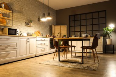 Mutfağın içinde tezgahlar, yemek masası ve akşam lambaları var.