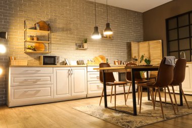 Mutfağın içinde tezgahlar, yemek masası ve akşam lambaları var.