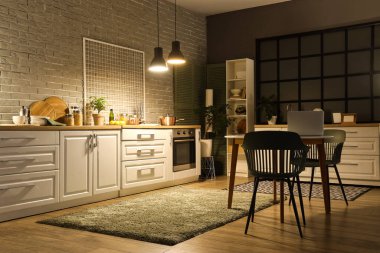 Akşamları tezgahları, yemek masası ve parlayan lambaları olan modern mutfak.