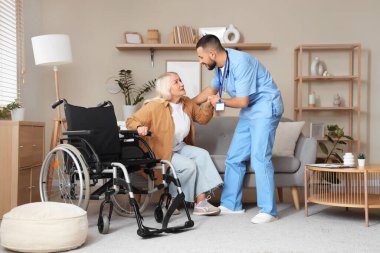 Erkek doktor olgun bir kadının evdeki kanepeden kalkmasına yardım ediyor.