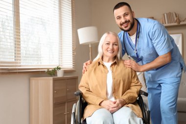 Evde tekerlekli sandalyede yetişkin bir kadınla erkek doktor.