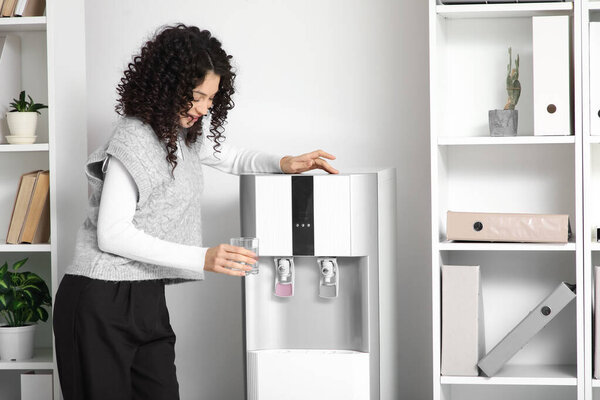 Young businesswoman pouring water from cooler in office