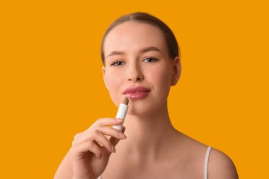 Turuncu arka planda dudak kremi olan güzel bir kadın.