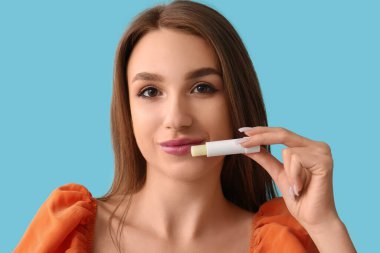 Mavi arka planda dudak kremi olan güzel genç bir kadın.