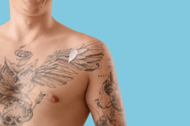 Mavi arka planda kremalı dövmeli genç adam, yakın plan.