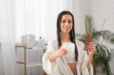 Bir kavanoz saç maskesi ve banyoda fırçası olan güzel, genç ve mutlu bir kadın.