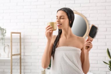 Bir kavanoz saç maskesi ve banyoda fırçası olan güzel, genç ve mutlu bir kadın.