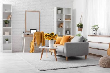 Oturma odasının içinde kanepe, işyeri ve sehpanın üzerinde ayçiçekleri var.