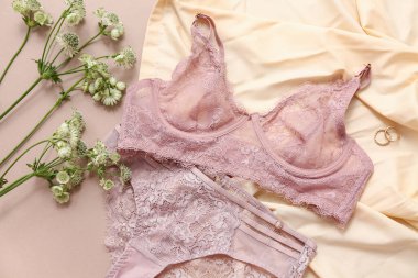 Renkli arka planda zarif kadın iç çamaşırları, küpeler ve çiçeklerle kompozisyon