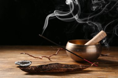 Yanan tütsü çubuğu ve koyu ahşap arka planda Tibet şarkı kasesi olan tutucu.