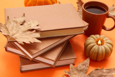 Farklı kitaplar, yanan mum, bir fincan çay ve akçaağaç yaprağı.