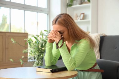 Evde boncuklarla ve İncil 'le dua eden olgun bir kadın.
