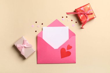 İçinde boş kart, kağıt kalpler ve bej arka planda hediye kutuları olan bir zarf. Sevgililer Günü kutlaması