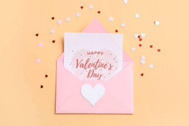 İçinde hediye kartı ve bej arka planda konfeti olan bir zarf. Sevgililer Günü kutlaması